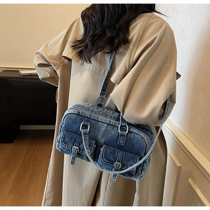 Close-up of blue denim Boston bag with buckle pockets on model in a beige trench coat