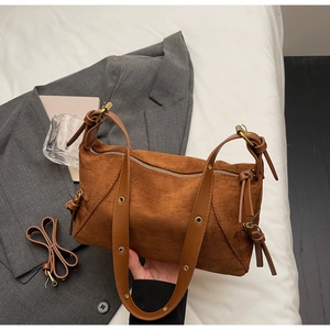 Detail of brown suede shoulder bag with side tassel and metal eyelet strap on grey blazer
