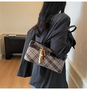 Detail of retro plaid underarm bag featuring brown leather straps and beaded charm accessory