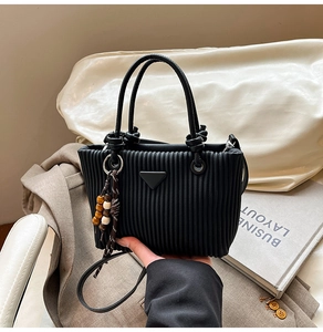 Détails d'un sac seau noir plissé avec plaque triangulaire en métal et charm en perles