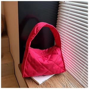 Detail of rose red quilted nylon handbag featuring diamond stitching on a wooden surface