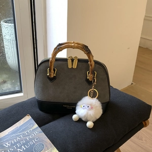 Detail of grey matte shell bag with bamboo handle and plush charm on black cushion