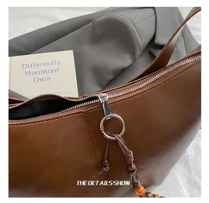 Macro shot of silver circular zipper pull and colorful beaded charm on brown leather bag