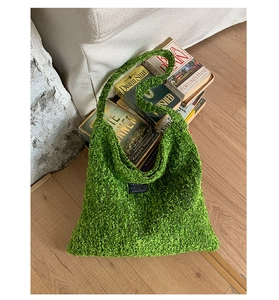 Detail van groene gebreide hobo tas met bouclé textuur en modelabel op een sfeervolle achtergrond