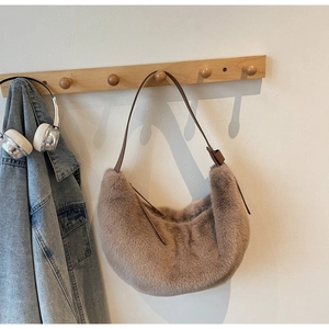 Detail view of plush apricot crescent bag with a leather strap on a wooden hook