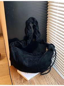 Black suede crescent hobo bag with unique ruched shoulder strap on wooden desk