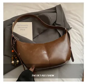 Detail of dark brown glossy leather hobo bag with wooden bead charm and wide strap