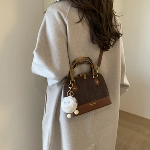 Detail of shell-shaped crossbody bag with bamboo handle and plush chick pendant