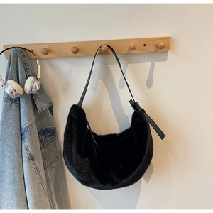 Detail of black faux fur hobo bag with a leather strap hanging on a wooden hook