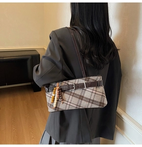 Detail of plaid shoulder bag featuring brown leather strap and decorative beaded charm