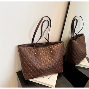 Detail view of large dark brown tote bag with quilted diamond pattern and golden rivets