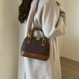 Detail view of contrast shell bag with bamboo handle and golden hardware on beige coat