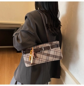 Detail view of a vintage plaid shoulder bag with leather strap and decorative beaded charm