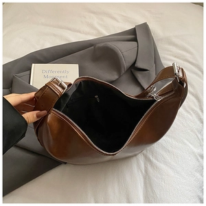 Minimalist brown crescent crossbody bag with adjustable strap on white bedding backdrop
