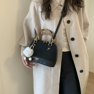 Detail of shell handbag with bamboo handle and plush charm on a beige wool coat