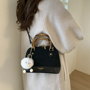 Detail of shell bag featuring bamboo handle, gold hardware, and plush charm accessory
