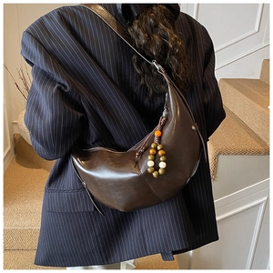 Detail of a dark brown crescent bag with a multi-colored beaded charm on a blazer