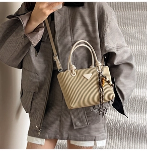Détail du sac seau plissé beige avec pompon en perles de bois et logo métallique