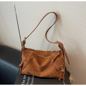 Close-up of brown suede dumpling bag with elongated knotted zipper pulls and leather strap
