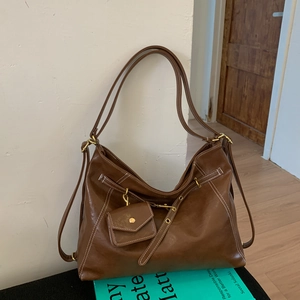 Détail macro du sac en cuir marron montrant les surpiqûres blanches et ferrures dorées