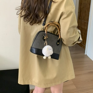 Deep grey shell bag with bamboo handles and a white pompom charm shown in a back view