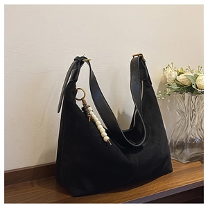 Detail of minimalist black suede moon bag with stylish beaded tassel and gold hardware