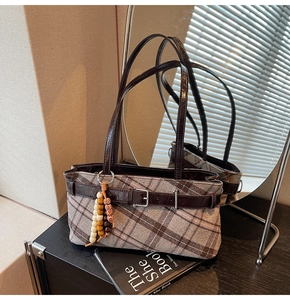 Detail of vintage plaid shoulder bag with dark leather strap and beaded charm on wood