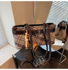 Detail of plaid shoulder bag featuring brown leather buckle and wooden bead charm
