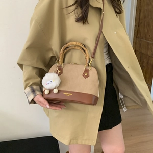 Detail of bamboo handle and sheep plush charm on a khaki shell bag in use