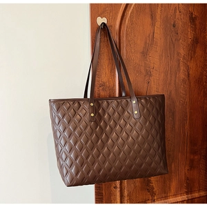 Detailed view of dark brown tote bag with quilted diamond pattern and gold rivets