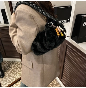 Detail of plush black shoulder bag with leather braided strap and ethnic beaded charm