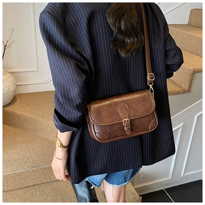 Detailed close-up of brown faux leather texture and golden metal buckle on crossbody bag
