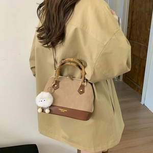 Elegant khaki shell bag with bamboo handles and pompom charm worn with trench coat