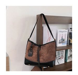 Close-up of suede tote bag featuring black leather trim and gold protective metal feet