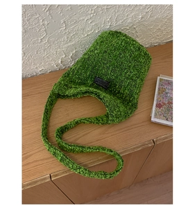 Detail der grünen Bouclé-Strick-Eimertasche mit Fashion-Label auf Holzoberfläche