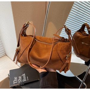 Detail of caramel brown suede handbag showing zipper closure and leather knot accents