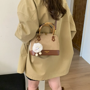 Detail of crossbody shell bag with bamboo handle and plush pendant on model