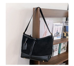 Detail of black suede tote with gold hardware hung on a dark wooden bookshelf