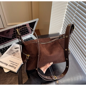 Detail of dark brown suede bag with gold zipper and eyelet leather strap on desk