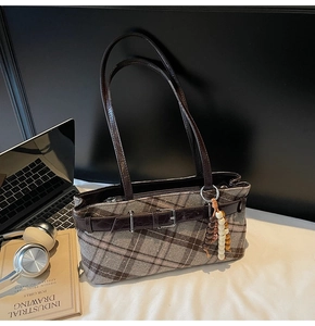 Detail view of plaid underarm bag with decorative belt buckle and ethnic beaded charm