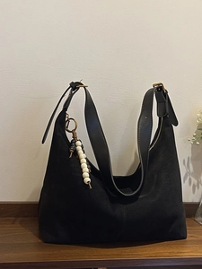 Sac hobo noir en daim avec bandoulière en cuir et breloque à pompon perlé sur une table
