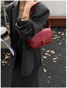 Close-up of retro red leather shoulder bag with buckle detail worn by a model in autumn