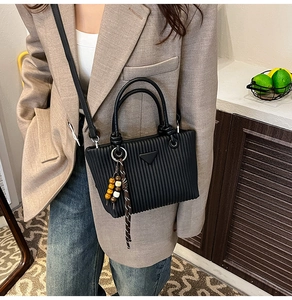 Détail du sac seau plissé noir avec logo triangle en métal et pompon en perles colorées