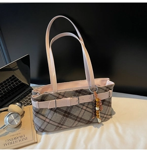 Detail of plaid tote bag with pink leather trim and wooden bead charm on office desk