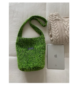 Detail einer grünen Plüsch-Beuteltasche mit schwarzem Modeetikett auf Stoffhintergrund