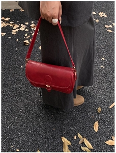 Detail view of red leather shoulder bag with gold buckle on autumn street background