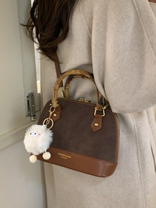 Premium brown shell bag with bamboo handle and plush charm worn on beige coat