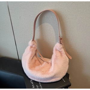 Detailed view of pink faux fur hobo bag with adjustable leather strap on a book
