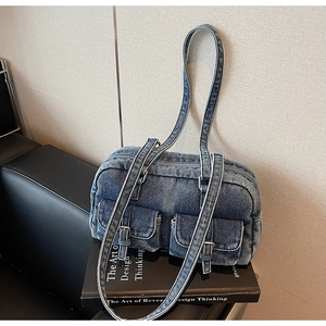 Close-up of blue washed denim shoulder bag with dual metal buckle flap pockets