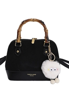 Elegant black shell handbag with bamboo handles and white pompom charm on white background